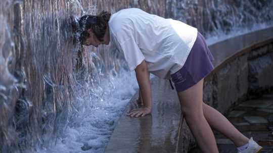 Žena sa ochladzuje vo fontáne počas horúčav v Moskve.