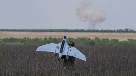 Ukrajinský vojak nesie dron, zatiaľ čo v pozadí stúpa dym po ruských náletoch na frontovej línii v Doneckej oblasti.