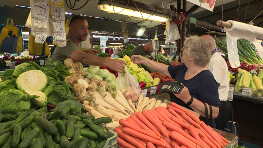 Trhovník na trhovisku Miletičova podáva zeleninu zákazníčke.