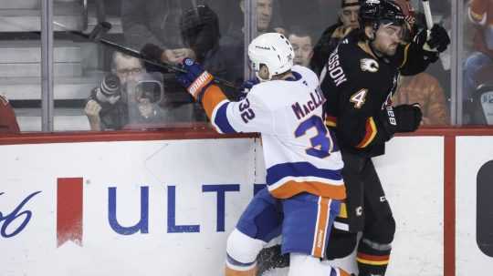 Zľava Kyle MacLean z New York Islanders v súboji o puk s Rasmusom Anderssonom z Calgary Flames.