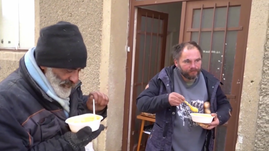Na snímke muži bez domova jedia polievku.